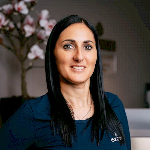 Bild zeigt eine lächelnde Mitarbeiterin von MK2WEI im blauen Obertteil und schwarzen Haaren.